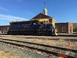 A blue and yellow diesel locomotive parked on railroad tracks, in front of a building.