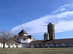 Two wings of a white barn with two silos under a blue sky with cirrus clouds