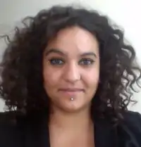 Portrait photo of a woman with curly brown hair, wearing a black blouse and chin jewelry.