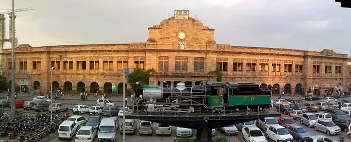 Low, tan building, with cars parked and a steam locomotive on display