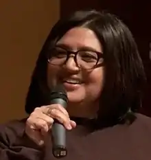 An woman with glasses is holding a microphone.