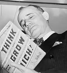 Photograph of the head of a man with head tilted and rested on the back of his right hand while reading a book