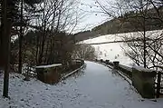 A snow-covered scene, lit by low sunlight, shows the footpath curving to the left before disappearing behind bare trees