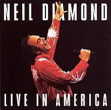 above the waist shot of a man in a red shirt singing with his left arm raised high (the man in red is Neil Diamond)