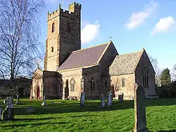 Stone building with prominent square tower. In the foreground are gravestones.