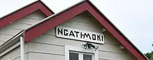 cropped image shows red roof line, weather board building and hand painted sign saying Ngati Moki