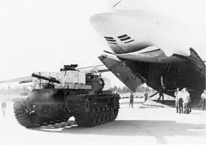 A cargo plane with its access door open, men, and a tank