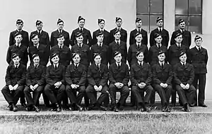 Three rows of men in dark military uniforms, wearing forage caps