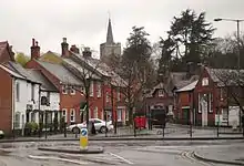 a number of buildings, mainly red, in front of a church on a hill and a row of big trees