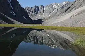 Still lake reflecting a steep, wide, rocky mountain ridge