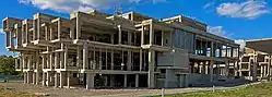 A three-quarters view of a skeletal structure of concrete beams and pillars, illuminated by the sun from the left.