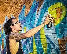 Orikal Uno painting a wall in Minneapolis in August 2023