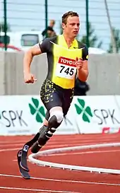 A man in a spandex singlet runs on a track. He has two prosthetics below the knees