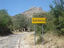 Traffic sign of the village and the steep rock in the background (south view)