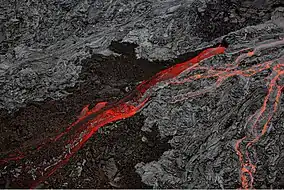 Aerial photograph of volcanic rock, with black cold lava split by a bright river of red lava