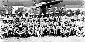 Three rows of uniformed men in front of a biplane