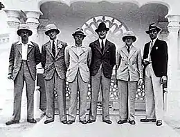 Thirteen men in dark military uniforms standing outside a building