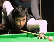 A photograph of a man playing Snooker wearing a white shirt and black waistcoat.