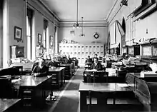 large room with center aisle and people sitting at several desks