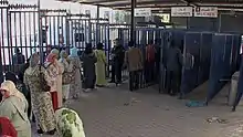 Gates labelled in Spanish and Arabic for "Men" and "Women" with queues of people in front of them.