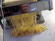 Dough being cut into noodles with a pasta machine