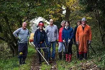 A path maintenance team, with tools, posing beside in a path flanked with trees