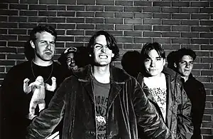 A black and white photograph of five members of the group Pavement standing in front of a brick wall