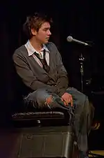 A man sits on a stool next to a microphone