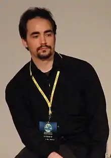 Peter Joseph wearing a dark shirt with a yellow lanyard, looking left of camera