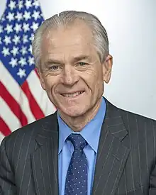 Navarro smiling, seated in front of an American flag