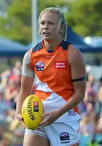 Female athlete in guernsey and shorts holds a football