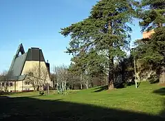 A southern view of the rear entrance to the church. In the foreground is playground equipment, a grass lawn and some trees.