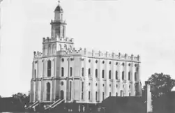 Black-and-white photograph of the St. George Temple. Like an especially ornate church. Looks smaller than a cathedral. Has a tower with a weather vane at the front. Two doors are at the front, with stairs leading up. Parapets line the roof, and ornate windows line the sides.