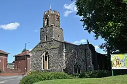 View of the church bathed in bright sunlight.  There is a 3-stage tower at the near end.