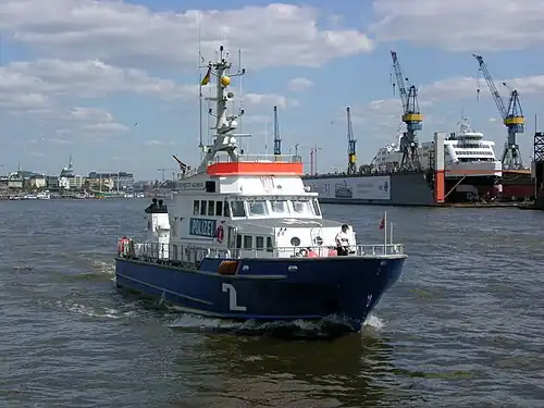 A boat with a blue hull and white deck. The name Bürgermeister Weichmann is written on the superstructures, also the German word for police. Police is written white letters on a blue field.)