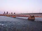 A steel box-girder bridge, with part of the city skyline in the background.