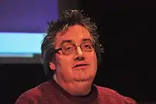 Close-up of a man with medium-length hair, glasses and a short goatee