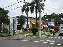 Several twinned buildings in a square with an ATM and among them the city hall, the municipal council hall, a bakery, and a shop