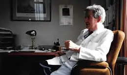 A man in a white coat sitting at a desk.