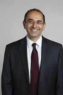 A man with a black suit and glasses smiling