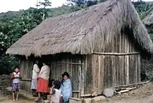 A Bolivian family stands next to a home built of reeds and palm fronds