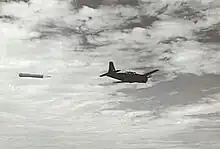 Black and white photo of a single-engined monoplane in flight. The aircraft is towing a piece of fabric.