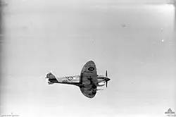 A black and white photograph of an aircraft with military style painting flying.