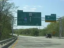 Ground-level view of two lanes of a divided freeway; two large, green exit signs are visible, and trees surround the freeway on both sides.