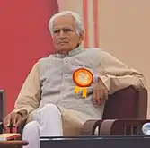 A photograph of an old man sitting in a chair with his leg crossed.