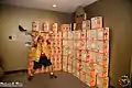 A wall of empty Maruchan ramen noodle boxes with a cardboard figure from Attack on Titan being swatted at by a member of Anime Midwest's staff