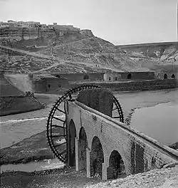 Ar-Rastan (on hill in background) and waterwheel (forefront) separated by Orontes River, 1930s