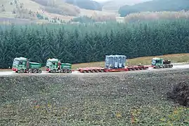 Two MAN SE ballast tractors pulling and one Mercedes pushing a 100,000 kg (220,000 lb) transformer on 10-axle lowboy