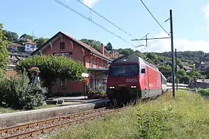 Red train on single-track line next to two-story building with gabled roof