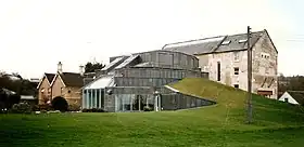 A large building with a rounded glass exterior built into the side of a low, sloping hill